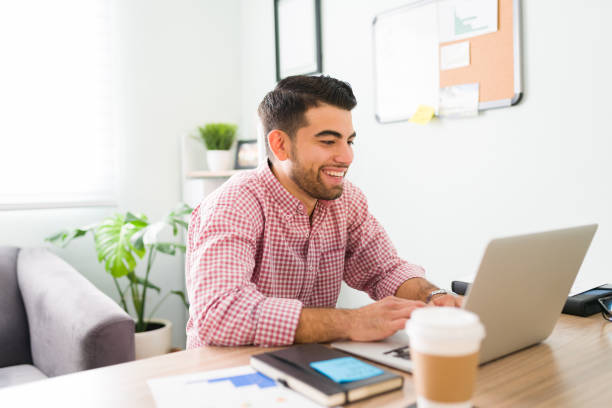 Happy latin salesman sitting at his home office desk and chatting during a videocall with co-workers